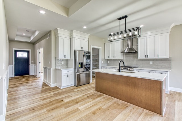 kitchen with white cabinetry, wall chimney range hood, stainless steel refrigerator with ice dispenser, and a kitchen island with sink