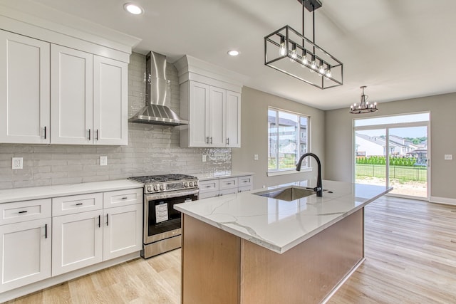 kitchen featuring stainless steel range with gas stovetop, white cabinetry, a kitchen island with sink, and wall chimney range hood