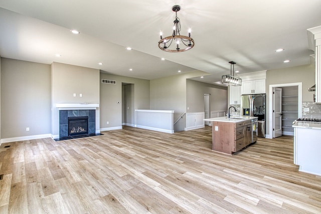 kitchen with a fireplace, pendant lighting, light hardwood / wood-style flooring, white cabinets, and an island with sink