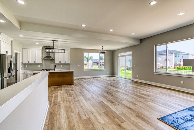 kitchen with white cabinets, wall chimney range hood, stainless steel refrigerator with ice dispenser, hanging light fixtures, and light wood-type flooring