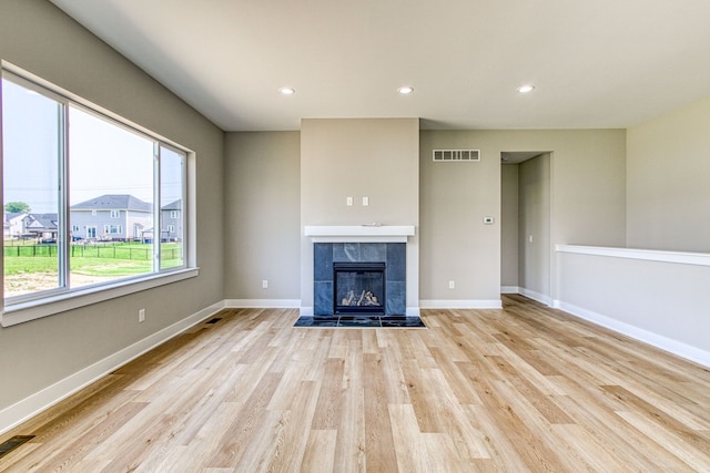 unfurnished living room with a tile fireplace and light hardwood / wood-style floors