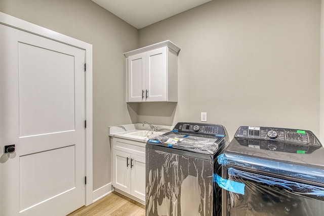 clothes washing area featuring washing machine and clothes dryer, sink, cabinets, and light hardwood / wood-style flooring