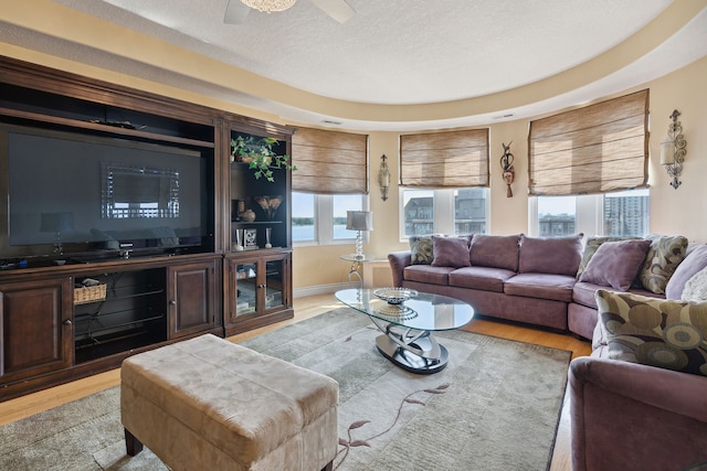 living room with a tray ceiling, ceiling fan, a textured ceiling, and light wood-type flooring