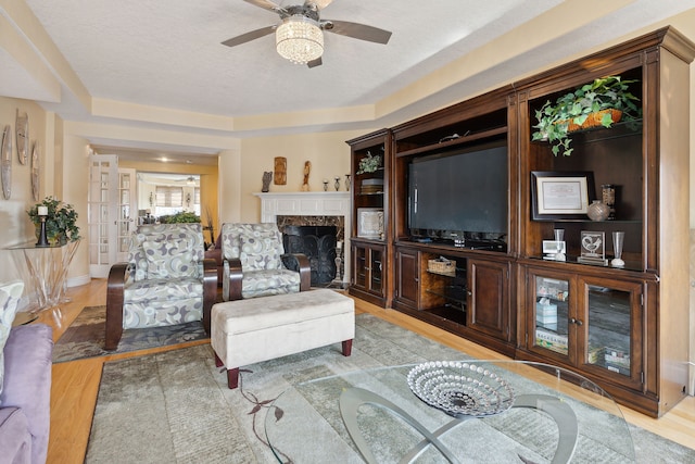 living room with ceiling fan, light hardwood / wood-style flooring, a high end fireplace, a textured ceiling, and a tray ceiling