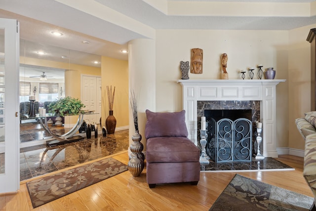 sitting room featuring a premium fireplace, light hardwood / wood-style flooring, ceiling fan, and a textured ceiling