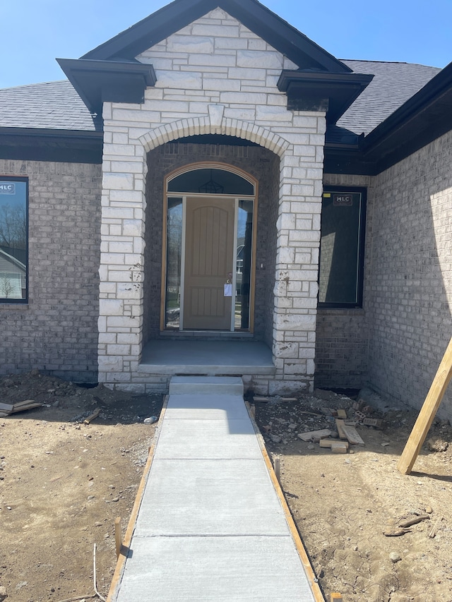 property entrance featuring brick siding, a shingled roof, and stone siding