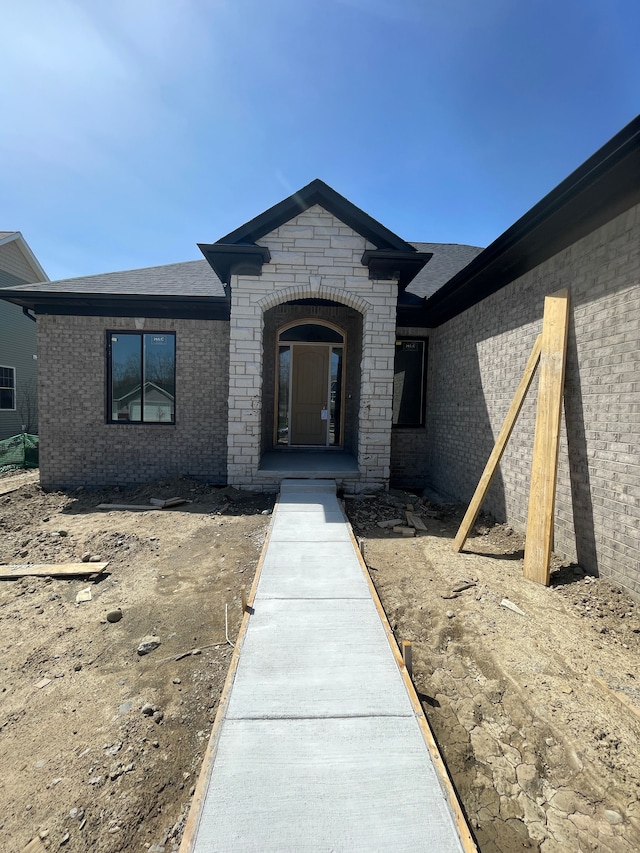 doorway to property with brick siding and roof with shingles