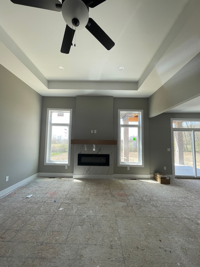 unfurnished living room with baseboards, a wealth of natural light, and a raised ceiling