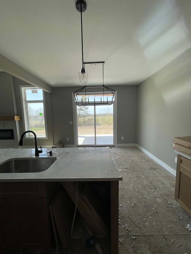 kitchen featuring baseboards, a sink, light stone counters, and a healthy amount of sunlight