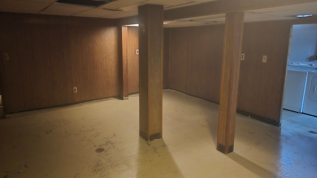 basement with a paneled ceiling, wood walls, and washing machine and dryer