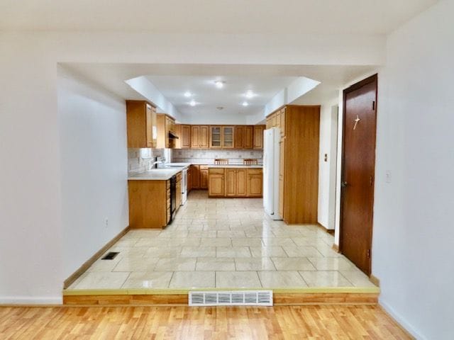 kitchen with white fridge, light hardwood / wood-style floors, a raised ceiling, and decorative backsplash