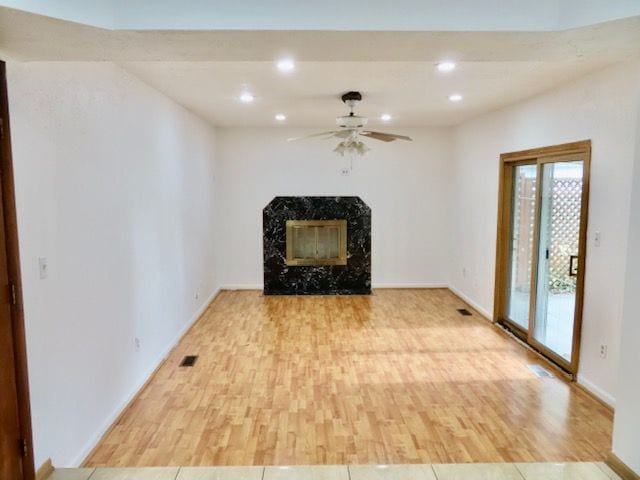 unfurnished living room with ceiling fan, a high end fireplace, and light wood-type flooring