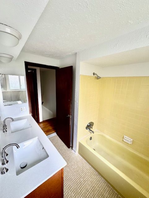 bathroom featuring vanity, a textured ceiling, and tiled shower / bath combo