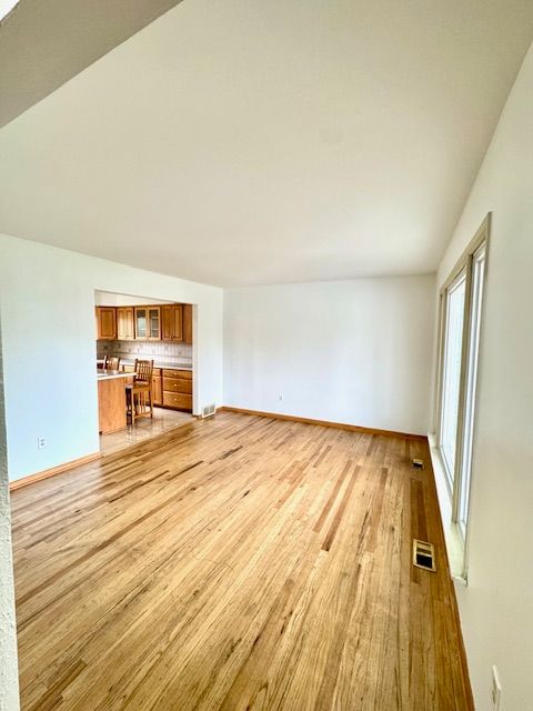 unfurnished living room featuring built in desk, light hardwood / wood-style floors, and vaulted ceiling