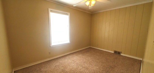 carpeted empty room featuring ornamental molding, ceiling fan, and wooden walls