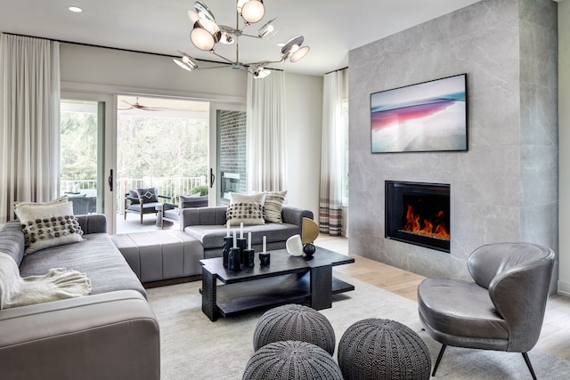 living room featuring ceiling fan with notable chandelier, light wood-type flooring, and a large fireplace