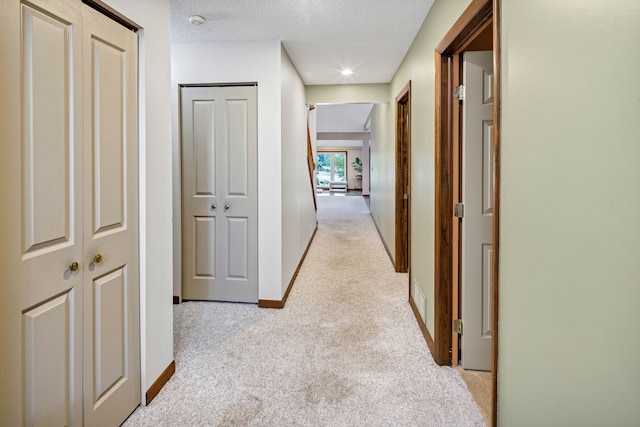 corridor with light carpet and a textured ceiling