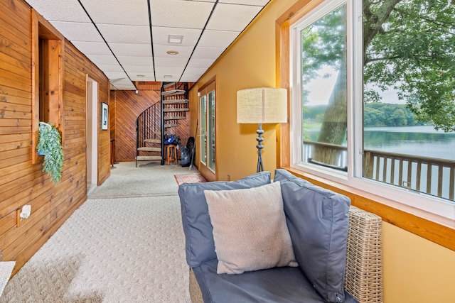 interior space with carpet, a paneled ceiling, wood walls, and a water view