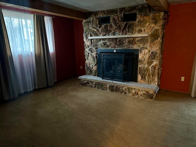 unfurnished living room with beamed ceiling, a stone fireplace, and carpet floors