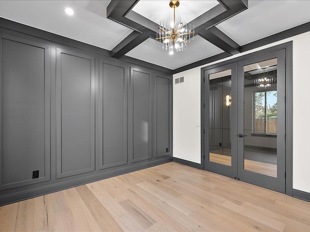 empty room with beam ceiling, an inviting chandelier, coffered ceiling, and light wood-type flooring