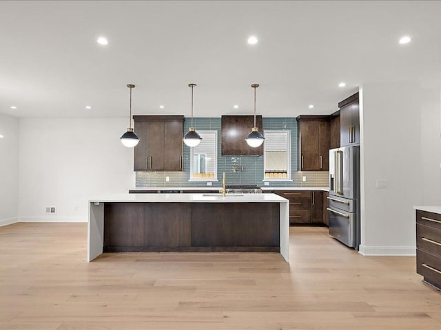 kitchen with high end refrigerator, dark brown cabinets, pendant lighting, and light hardwood / wood-style floors