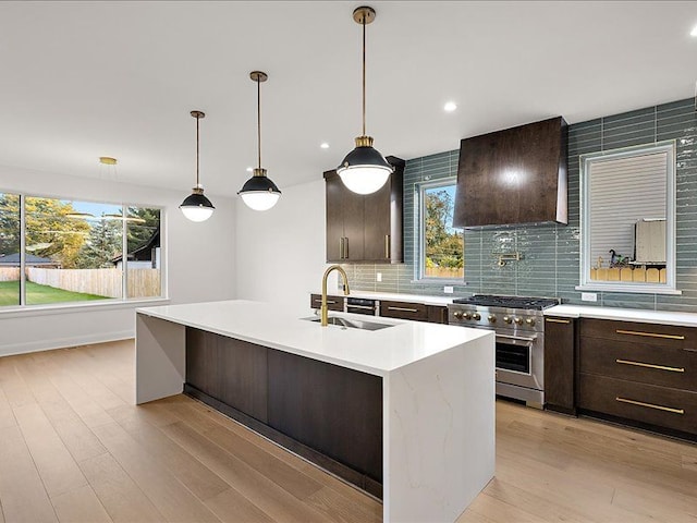 kitchen with high end stove, sink, a center island with sink, light hardwood / wood-style floors, and range hood