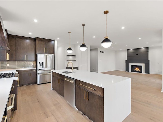 kitchen featuring sink, a center island with sink, light hardwood / wood-style flooring, high quality appliances, and hanging light fixtures