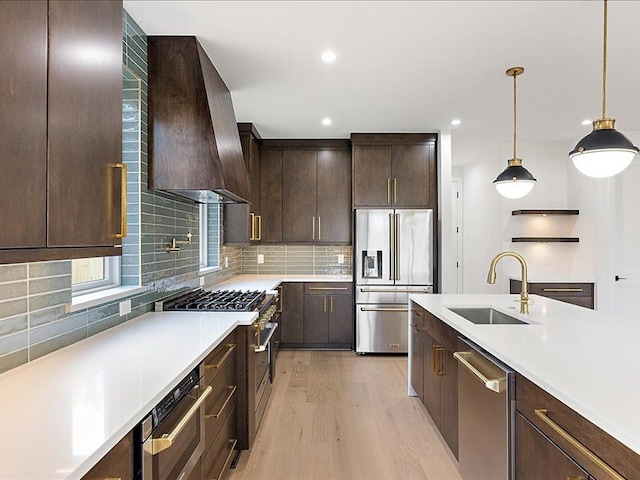 kitchen with pendant lighting, wall chimney range hood, sink, light hardwood / wood-style flooring, and premium appliances