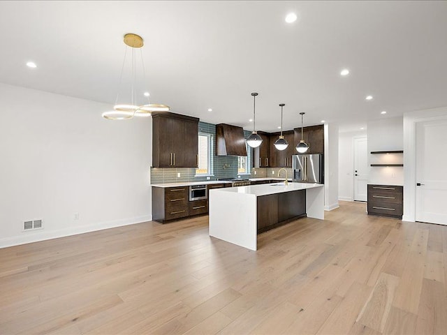 kitchen with appliances with stainless steel finishes, dark brown cabinetry, light hardwood / wood-style flooring, and pendant lighting