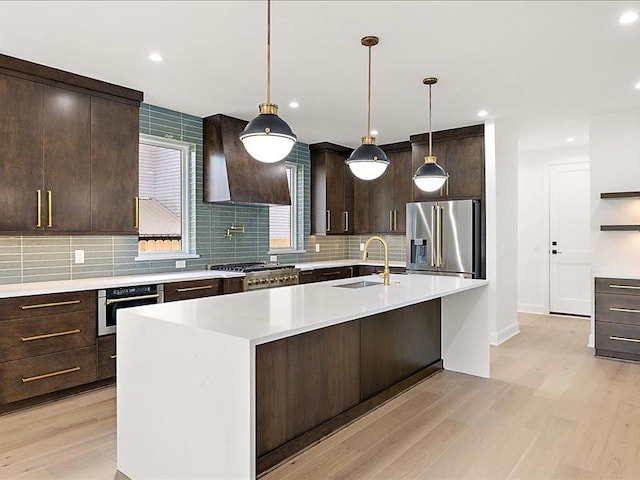 kitchen with a kitchen island with sink, wall chimney range hood, sink, decorative light fixtures, and stainless steel appliances