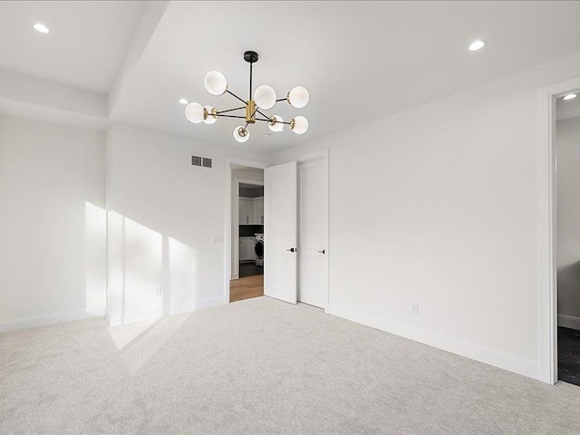 carpeted spare room featuring washer / clothes dryer and a chandelier