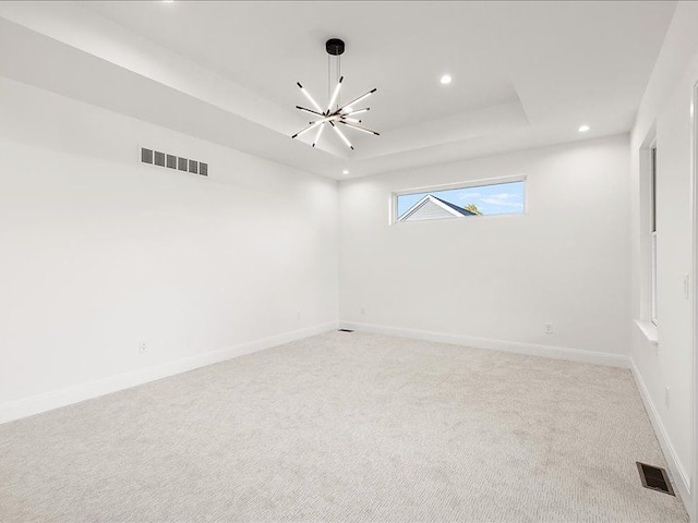 carpeted empty room featuring a chandelier and a tray ceiling