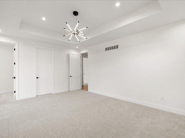 spare room featuring light carpet, a tray ceiling, and an inviting chandelier