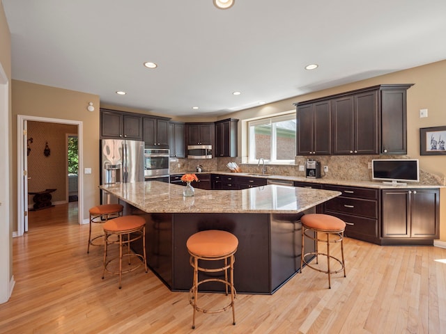 kitchen featuring a kitchen breakfast bar, a spacious island, appliances with stainless steel finishes, light hardwood / wood-style floors, and light stone counters