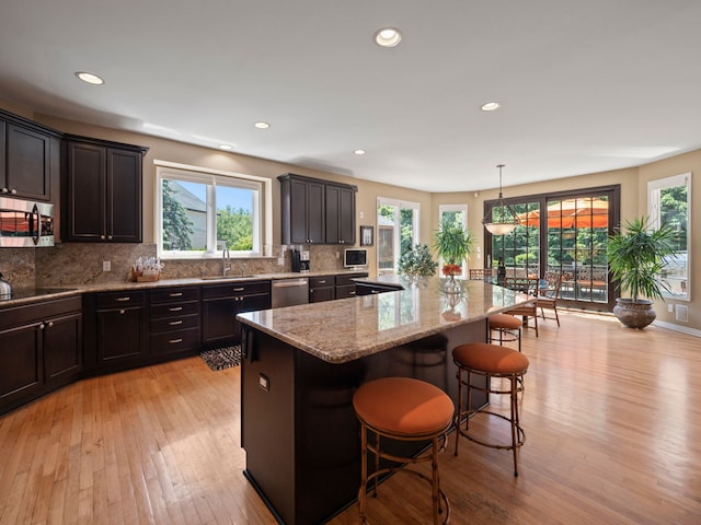 kitchen with a center island, hanging light fixtures, a breakfast bar area, light wood-type flooring, and stainless steel appliances