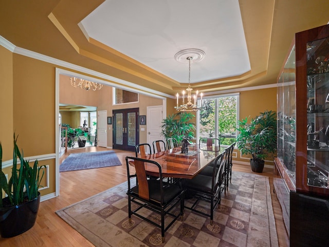 dining space featuring wood-type flooring, a tray ceiling, crown molding, and a notable chandelier