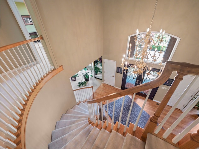 staircase featuring hardwood / wood-style floors, a notable chandelier, and a towering ceiling