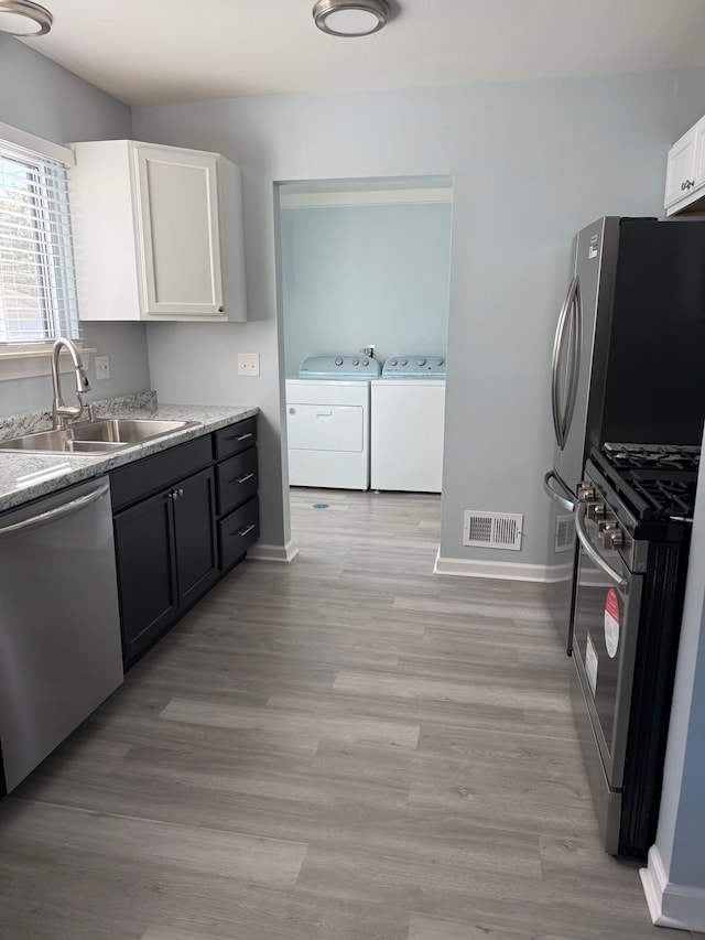 kitchen with appliances with stainless steel finishes, sink, washer and dryer, light hardwood / wood-style flooring, and white cabinetry