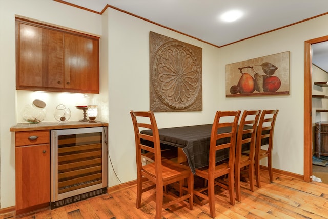 dining area featuring bar, ornamental molding, beverage cooler, and light wood-type flooring