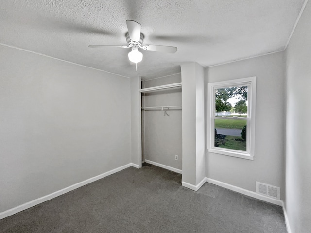 unfurnished bedroom featuring dark colored carpet, ceiling fan, a textured ceiling, and a closet