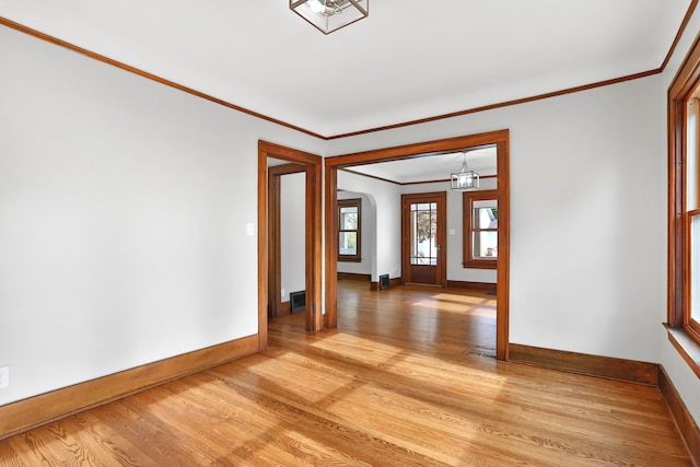 empty room with an inviting chandelier, ornamental molding, and light hardwood / wood-style flooring