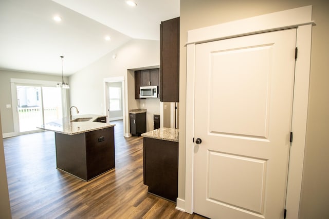 kitchen with sink, light stone counters, dark hardwood / wood-style floors, lofted ceiling, and a kitchen island with sink