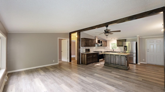 kitchen with stainless steel appliances, wall chimney range hood, lofted ceiling with beams, hardwood / wood-style floors, and a kitchen island