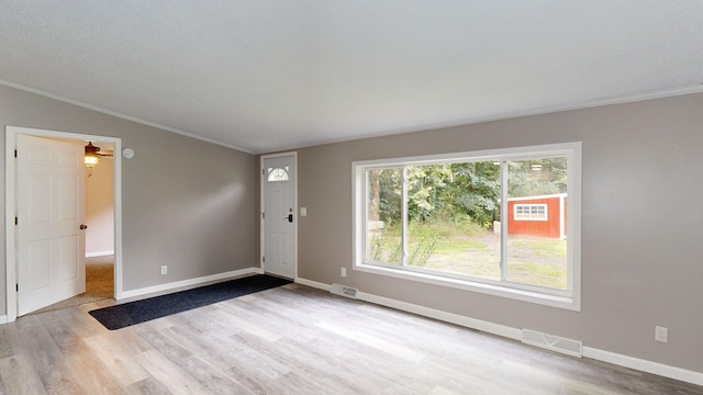 empty room with a textured ceiling, light hardwood / wood-style floors, crown molding, and lofted ceiling