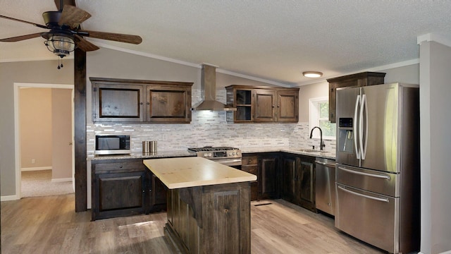 kitchen featuring sink, stainless steel appliances, wall chimney range hood, vaulted ceiling, and a kitchen island