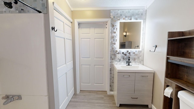 bathroom featuring tasteful backsplash, wood-type flooring, toilet, vanity, and ornamental molding