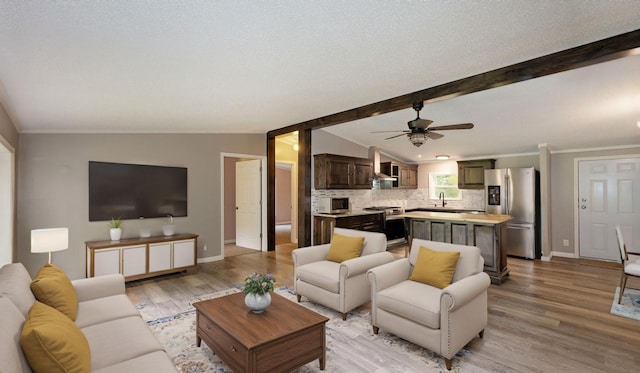 living room featuring ceiling fan, sink, lofted ceiling with beams, a textured ceiling, and light wood-type flooring