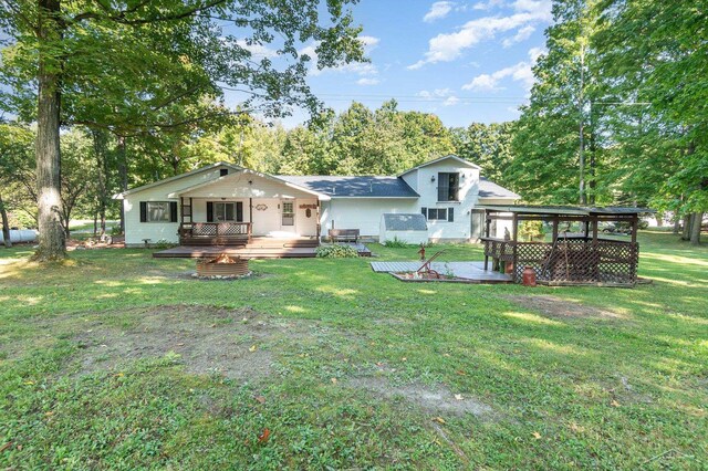 6610 E Arnold Lake Rd, Harrison, MI 48625 - rear view of house featuring a deck, an outdoor fire pit, a lawn, and view of wooded area