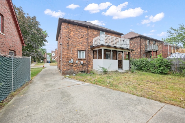 back of property featuring a lawn, a sunroom, and a balcony