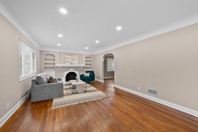 living room with hardwood / wood-style floors, built in features, a fireplace, and ornamental molding